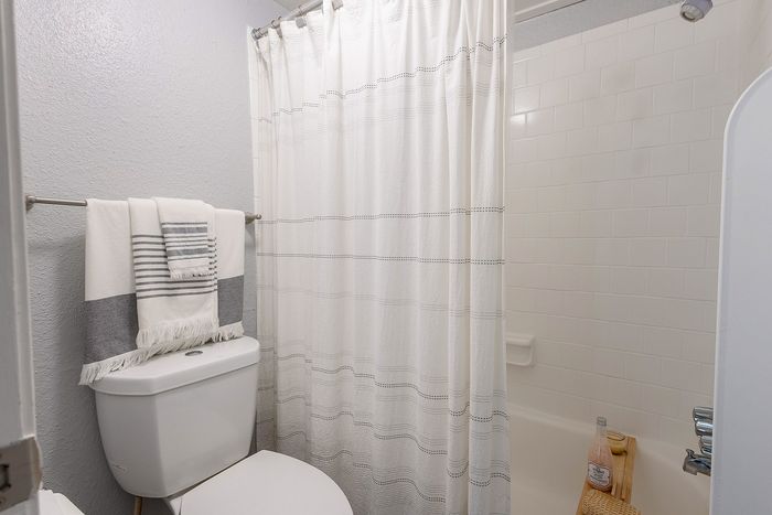 Bathroom with tub and shower combination, white tile surround, and neutral finishes