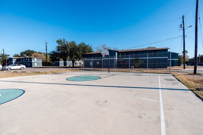 Inviting community with outdoor basketball court, surrounded by modern apartment buildings and lush trees, under a clear blue sky.