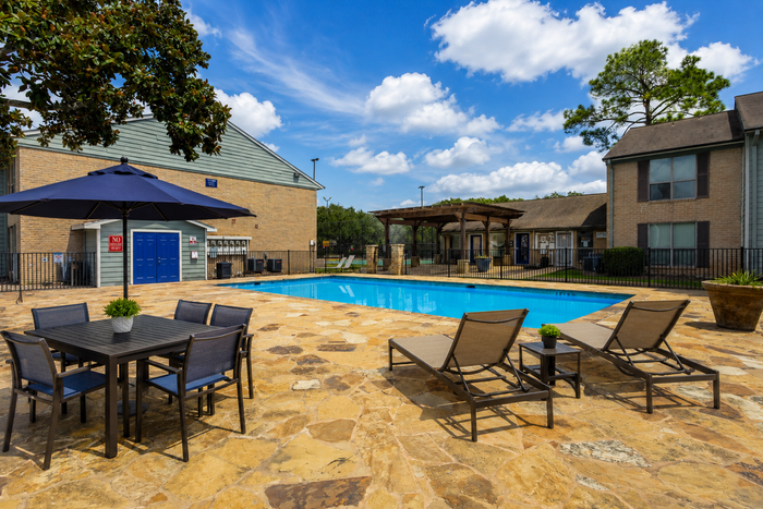 Swimming pool and sundeck with outdoor lounge seating at Westwood Village Apartments in Rosenberg, TX