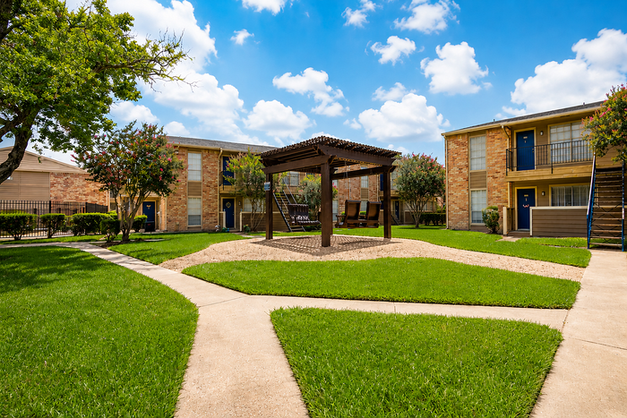 Outdoor swing lounge and landscaped courtyard at Newport Oaks Apartments in Alvin, TX with green space and shaded seating.