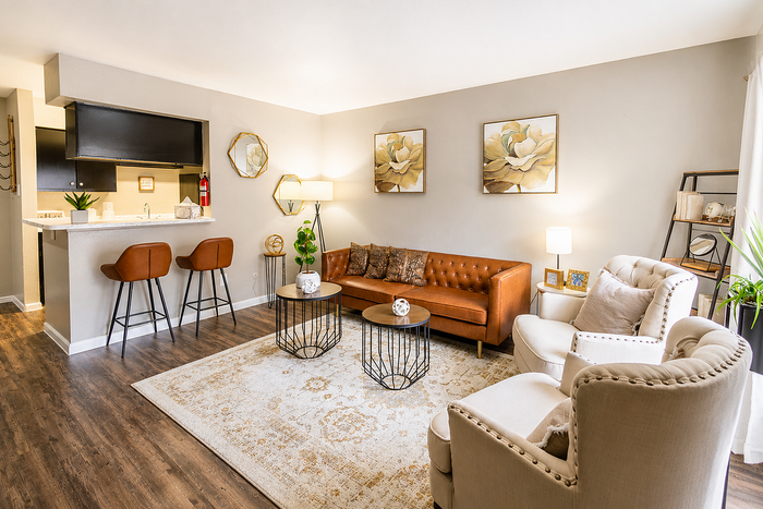 Elegant living room with soft lighting, featuring a stylish leather sofa, plush armchairs, and a chic kitchenette with bar stools.