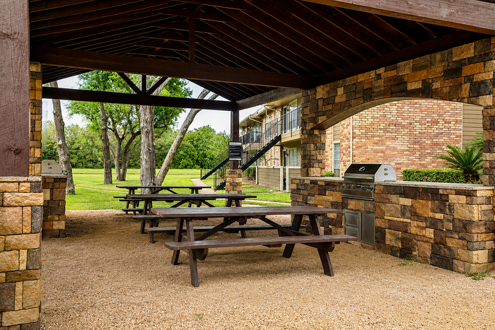 Outdoor kitchen and covered picnic pavilion at Newport Oaks Apartments in Alvin, TX featuring grilling stations, shaded seating, and landscaped gathering areas.