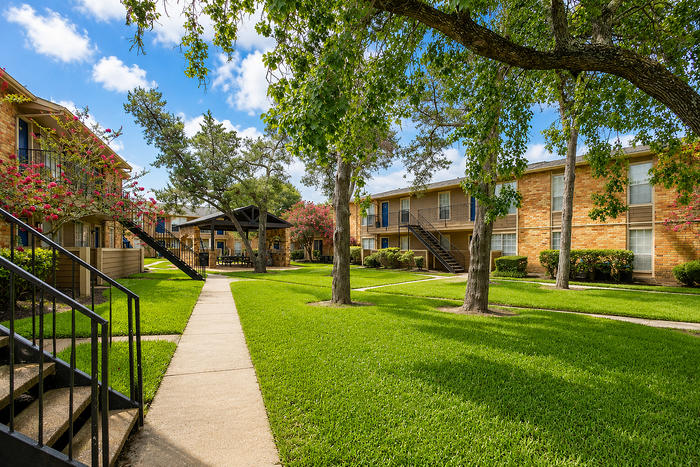 Landscaped courtyard walkway at Newport Oaks Apartments in Alvin, TX with mature trees and well-maintained green space.