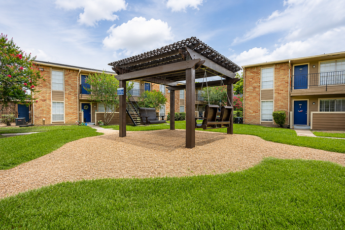 Outdoor swing lounge and landscaped courtyard at Newport Oaks Apartments in Alvin, TX with green space and shaded seating.