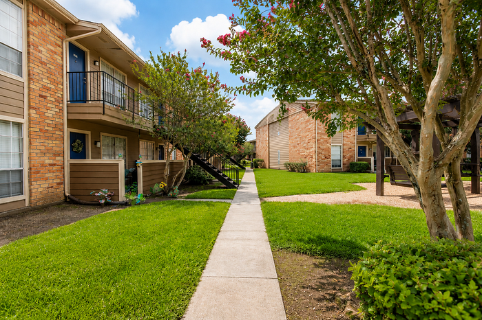 Landscaped courtyard and walking paths at Newport Oaks Apartments in Alvin, TX with maintained green spaces and mature trees.