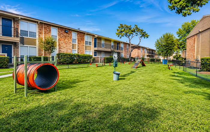 Fenced dog park with agility equipment and open green space at Newport Oaks Apartments in Alvin, TX.