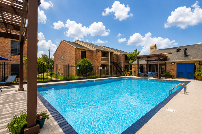 Resort-style swimming pool with lounge seating and shaded pergolas at Brookmore Hollow Apartments in Rosenberg, TX.