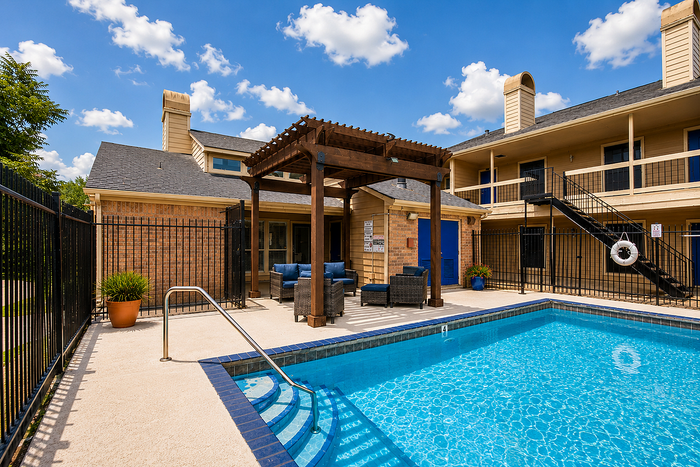 Community swimming pool with shaded lounge area and outdoor seating at Brookmore Hollow Apartments.