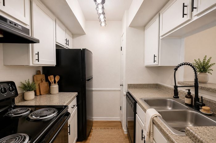 Deerbrook Gardens apartment kitchen in Humble, TX with white cabinetry, black appliances, double sink and granite-look countertops.