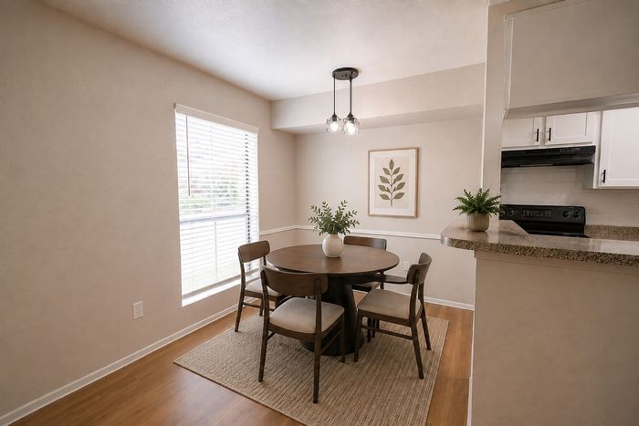 Elegant dining areOpen dining space in a Deerbrook Gardens apartment in Humble, TX with wood dining furniture, neutral d&eacute;cor and kitchen access.a with round table, chic pendant lighting, and large window for natural light.