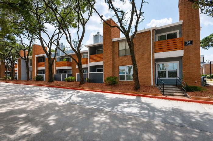 Deerbrook Gardens apartment building in Humble, TX with brick exterior, blue-gray accents, private patios and wood balconies.
