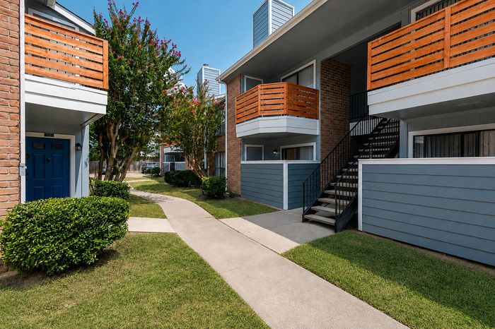 Courtyard-side apartment buildings at Deerbrook Gardens in Humble, TX with mature landscaping, walkways and updated balcony enclosures.