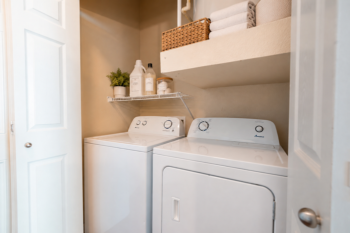 In-home laundry area at Oak Tree Apartments in Kingsville, TX, with full-size washer and dryer and additional storage shelving.