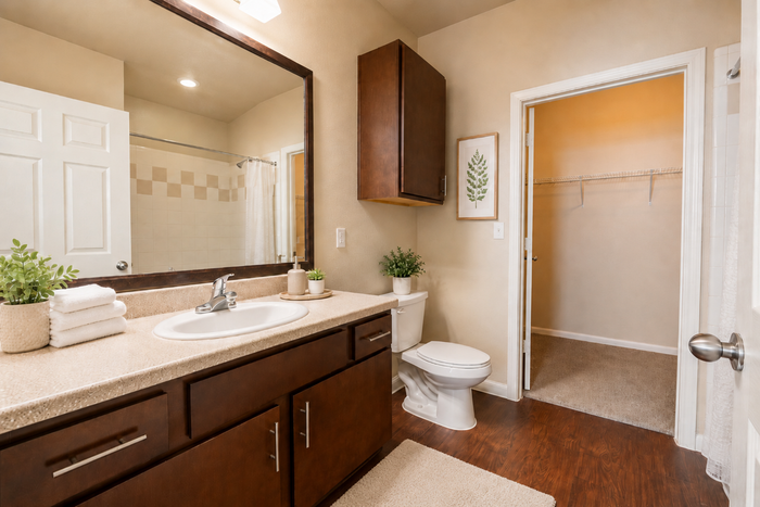 Bathroom at Oak Tree Apartments in Kingsville, TX, featuring a spacious vanity, dark wood cabinetry, large mirror and adjoining closet.