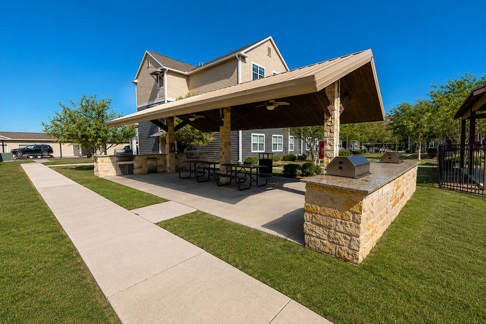Inviting outdoor pavilion featuring a large covered seating area with built-in grills, surrounded by lush greenery and clear blue skies.