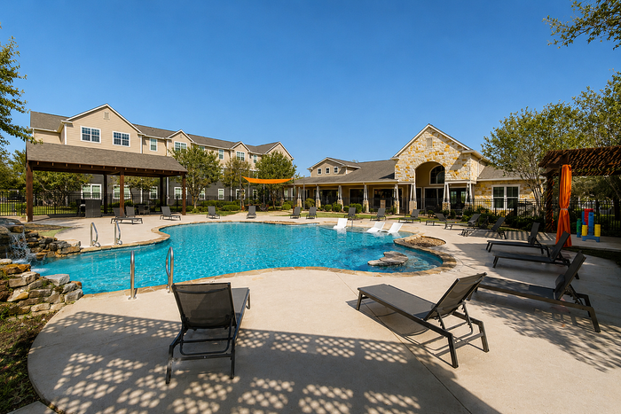 Luxurious apartment complex showcasing a sparkling pool with sun loungers and elegant architecture under a clear blue sky.