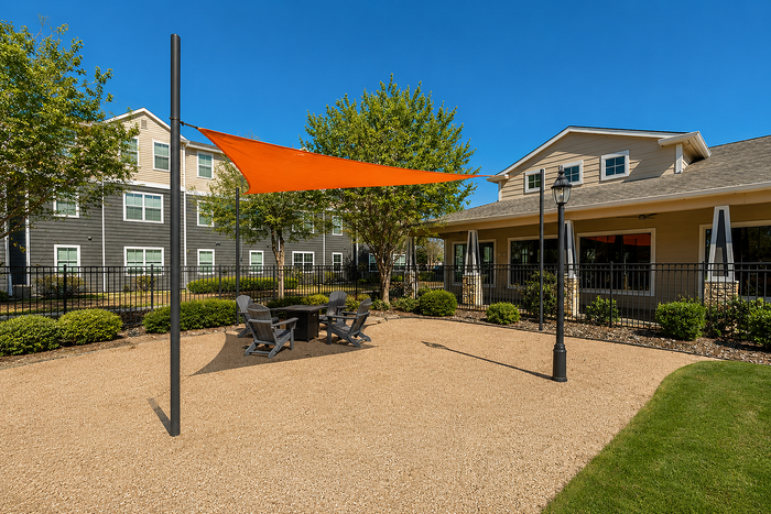 Charming outdoor patio area with orange sunshade and stylish seating, surrounded by lush greenery and modern architecture.