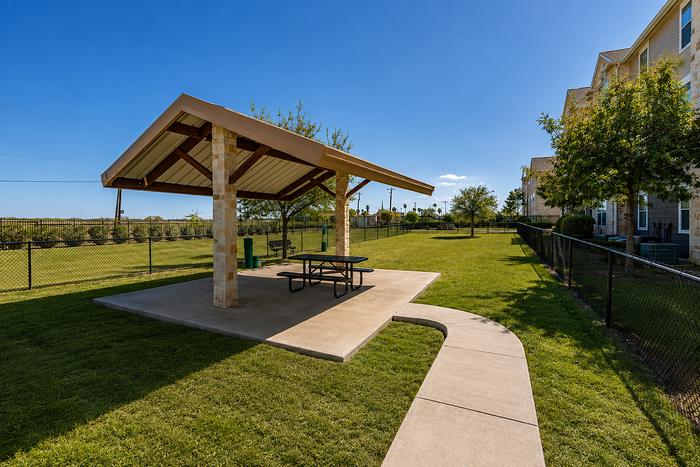 Charming community area with a covered picnic pavilion, lush green lawns, and neighboring buildings in a serene environment.