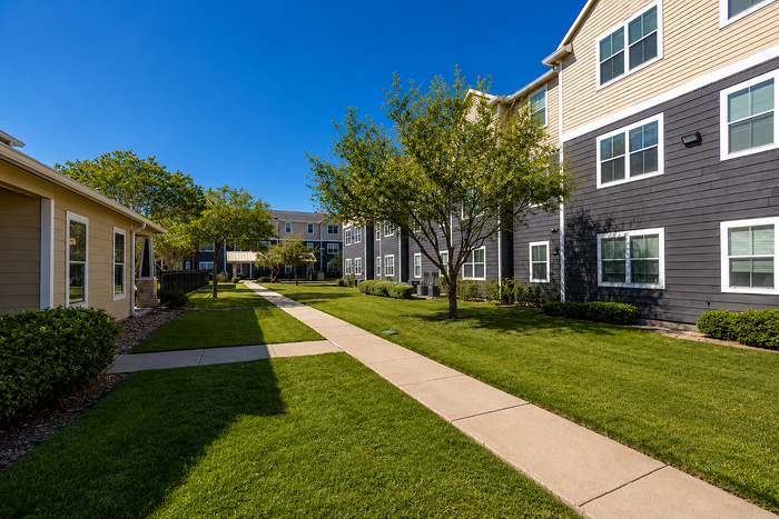 Inviting apartment complex featuring manicured lawns, mature trees, and modern exterior design under a clear blue sky.