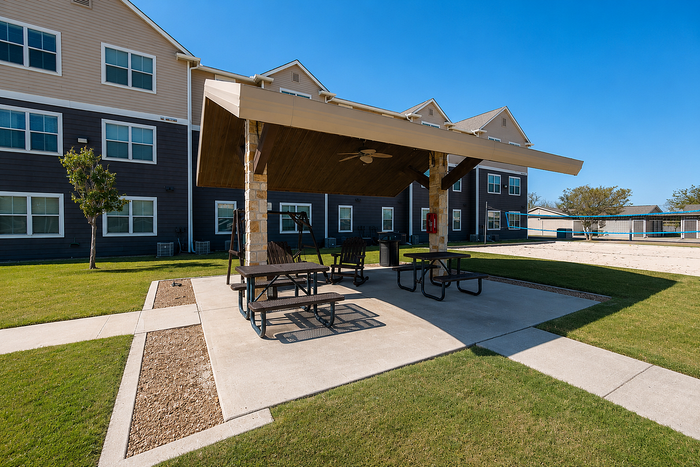 Inviting outdoor patio area with shaded seating, perfect for gatherings, surrounded by well-maintained lawns and modern apartment buildings in the background.