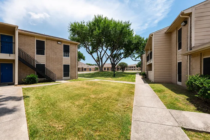 Landscaped apartment courtyard with mature trees, sidewalks and two-story residential buildings at The Reserve on Garth in Baytown, TX.