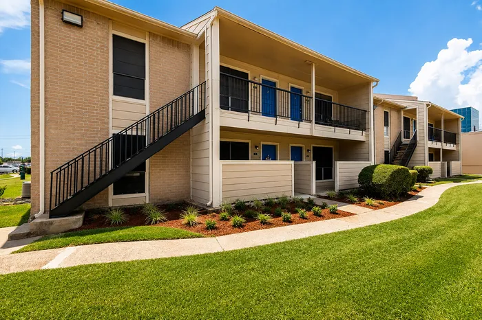 Two-story apartment building with blue entry doors, exterior staircase and landscaped grounds at The Reserve on Garth in Baytown, TX.