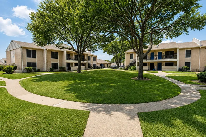 Landscaped apartment courtyard with mature trees, sidewalks and two-story residential buildings at The Reserve on Garth in Baytown, TX.