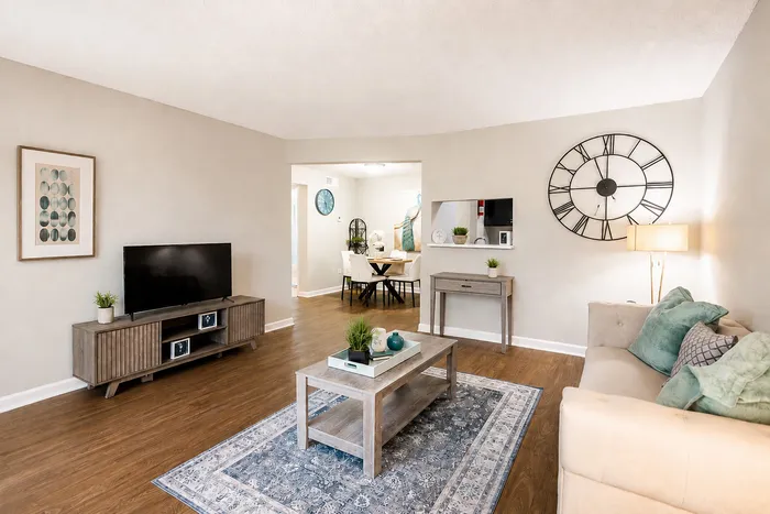 Furnished apartment living room with wood-style flooring, neutral seating, area rug and adjoining dining area at The Reserve on Garth in Baytown, TX.