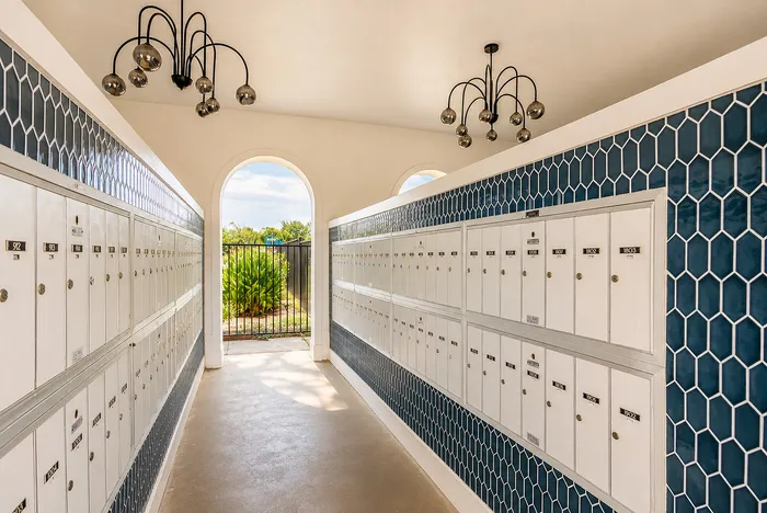 Covered resident mail center with rows of individual mailboxes and blue geometric tile accents at The Reserve on Garth in Baytown, TX.