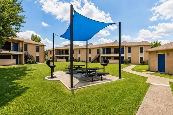Community picnic area with blue shade canopy, picnic tables and barbecue grills at The Reserve on Garth apartments in Baytown, TX.