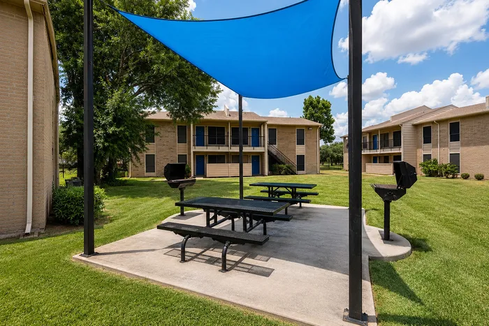 Shaded outdoor amenity area with picnic tables and community grills surrounded by apartment buildings at The Reserve on Garth.
