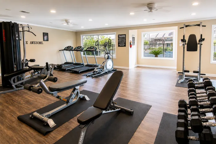 Fitness center with treadmills, elliptical equipment, strength-training machines, benches and dumbbells at The Reserve on Garth apartments in Baytown, TX.