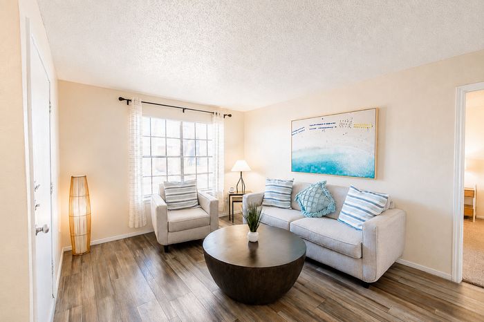Furnished living room at Apple Creek apartments in Kingsville, TX with wood-style flooring, sofa, accent chair and large window.