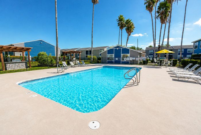 Community pool at Apple Creek in Kingsville with lounge chairs, outdoor seating and palm trees surrounding the pool deck.