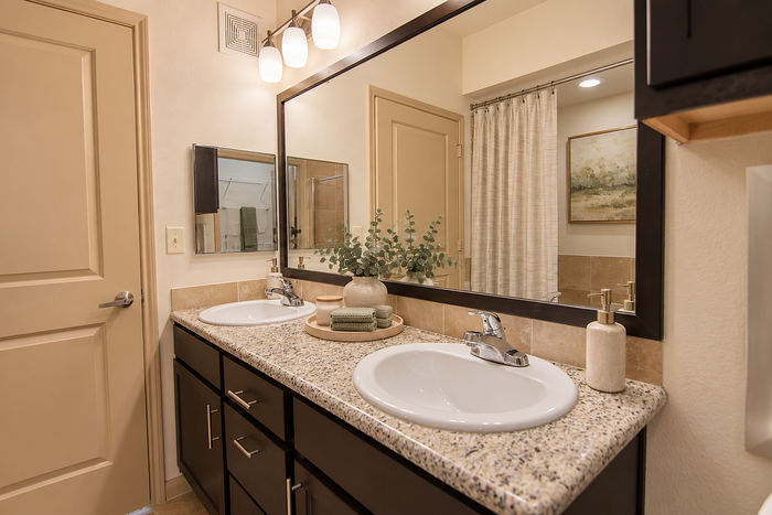 Bathroom at Valencia Place apartments in Houston, TX featuring a double vanity, granite countertop, dark cabinetry and neutral decor.