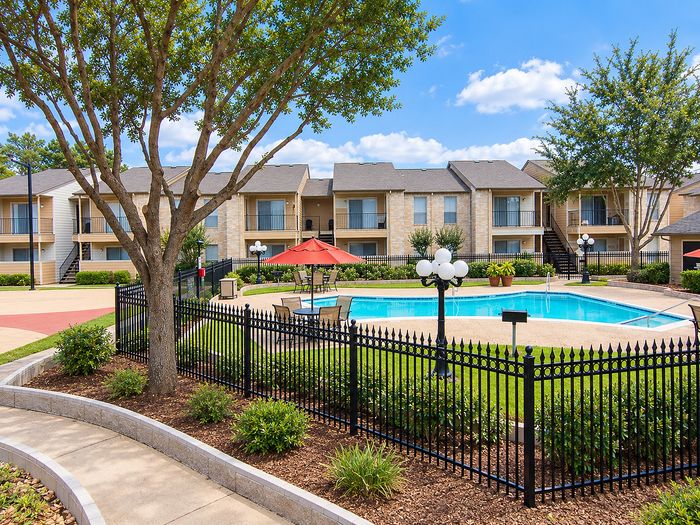 Community pool with patio seating, red umbrellas, landscaping and apartment buildings at Parkside Apartments.