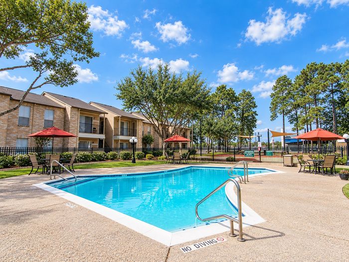 Outdoor swimming pool with patio seating, red umbrellas and apartment buildings at Parkside Apartments.