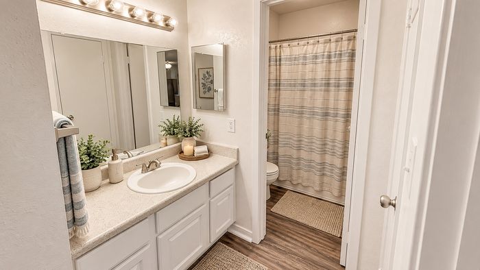 Apartment bathroom with white vanity, large mirror, tub and neutral decor at Parkside Apartments.