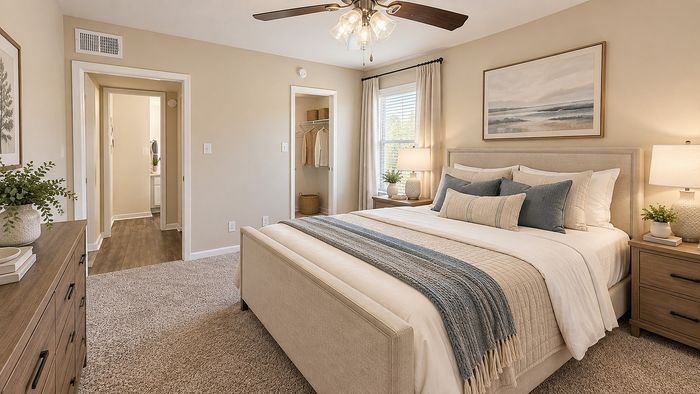Staged bedroom with neutral upholstered bed, wood nightstands, window and walk-in closet at Parkside Apartments.