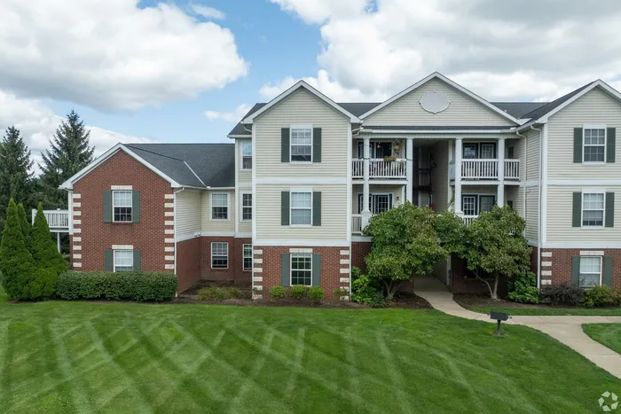 Charming apartment building with classic brick facade and manicured green lawns, offering serene living surrounded by nature.