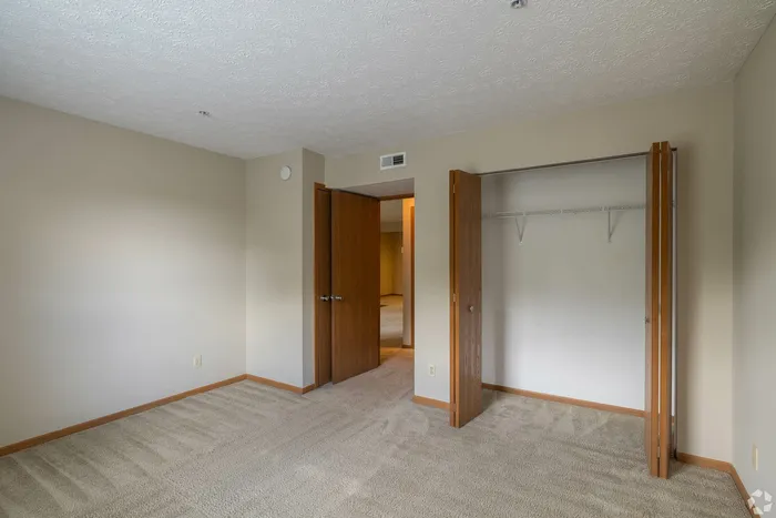 Bright and inviting bedroom with soft carpet and spacious closet featuring wooden bifold doors, perfect for comfortable living.