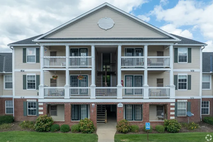 Charming apartment building with classic brick and beige siding, featuring inviting balconies and lush landscaping under a clear blue sky.