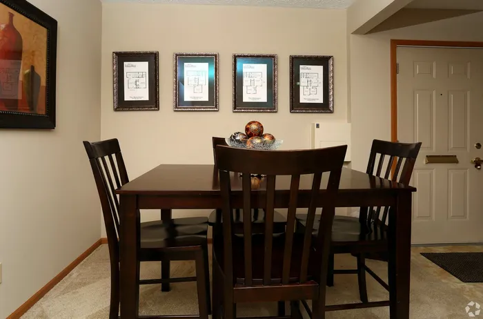Elegant dining area with dark wood furniture and artistic framed floor plans, creating a cozy and sophisticated ambiance.