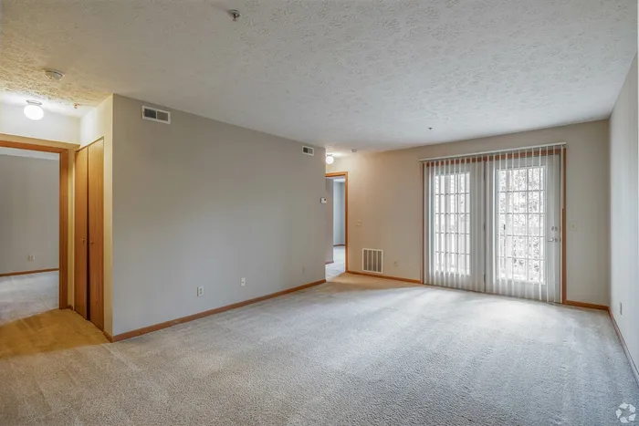 Bright and spacious living area with plush carpet and sliding glass doors opening to a natural light-filled balcony.