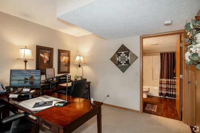 Inviting home office with elegant decor, rich wooden desk, and ambient lighting, leading to a stylish bathroom with modern finishes.