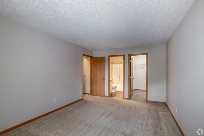 Bright bedroom with plush carpeting, featuring a bathroom and spacious walk-in closet, perfect for modern living.