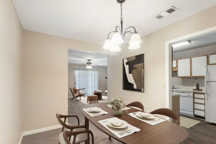 Bright, open-concept dining and living area with elegant lighting, modern artwork, and cozy furnishing; adjacent to a well-equipped kitchen with white cabinetry.