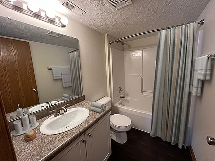 Modern bathroom with elegant vanity, spacious mirror, and a sleek shower-tub combo featuring soft lighting for a serene ambiance.