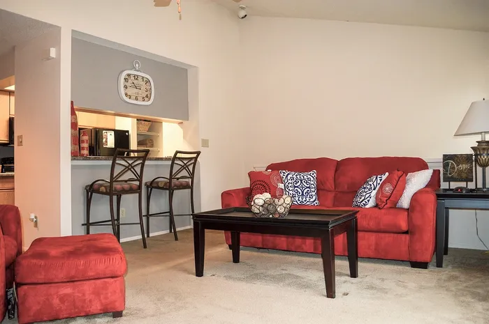 Inviting living space featuring vibrant red sofas, elegant bar stools, and an open breakfast bar, perfect for comfort and style.
