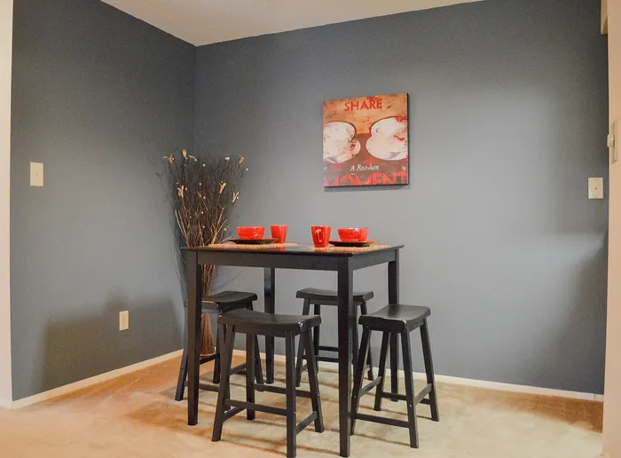 Charming dining nook featuring a sleek black table set with vibrant red dishes, complemented by a modern art piece on soothing gray walls.